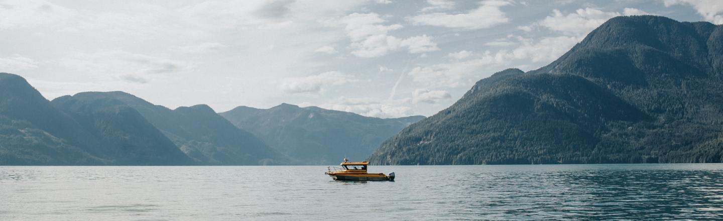 A small fishing boat in a big lake surrounded by rolling green hills.