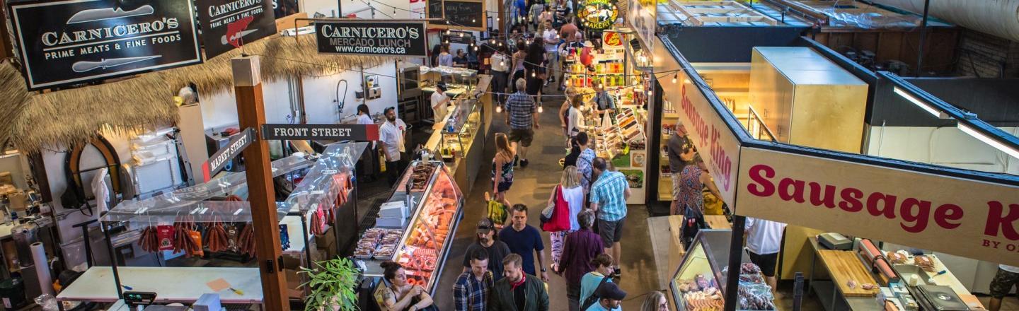 A bustling indoor farmer's market full of stalls and patrons