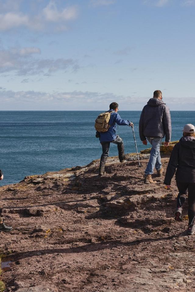 Four hikers walking along a rocky coastal cliff overlooking the ocean