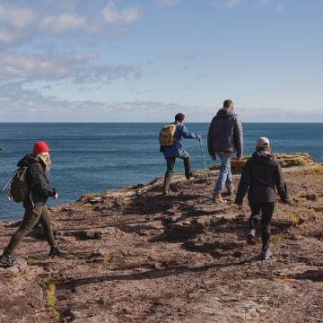 Quatre personnes marchent le long d’une falaise rocheuse qui donne sur l’océan.